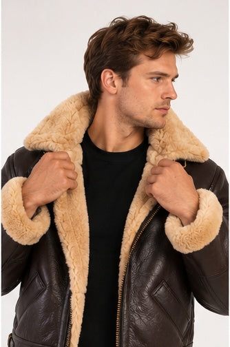 A man wearing a dark brown leather aviator jacket with a thick beige shearling collar, holding the collar open against a light gray studio background.