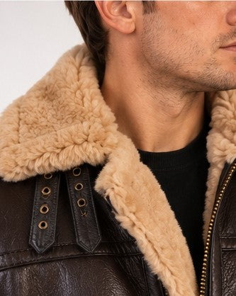 Close-up of a person wearing a dark brown leather aviator-style jacket with a thick beige shearling collar over a black shirt.